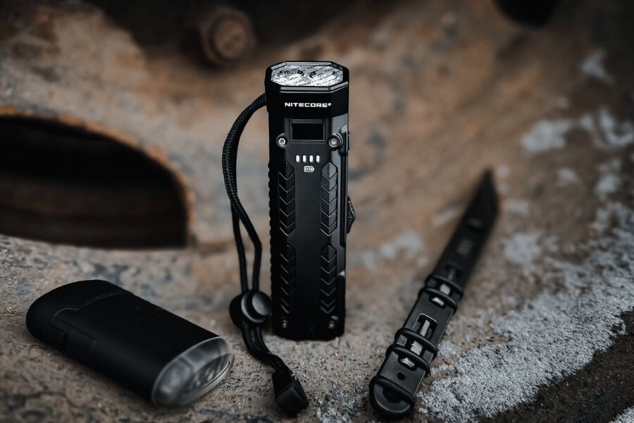 EDC gear including a Nitecore flashlight, folding knife, and other everyday carry essentials laid out on a concrete surface.