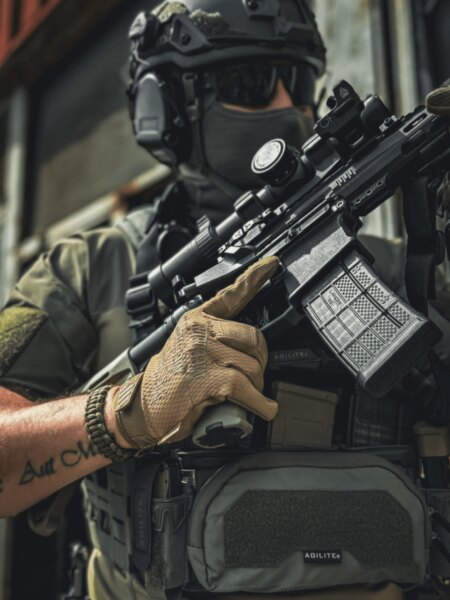Close-up of a shooter in tactical gear holding a PCC equipped with an optic and magazine.