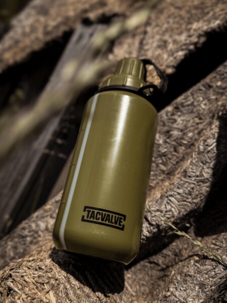 Green TacValve<sup>&reg;</sup> ModCan military canteen placed on a wooden surface in an outdoor setting.