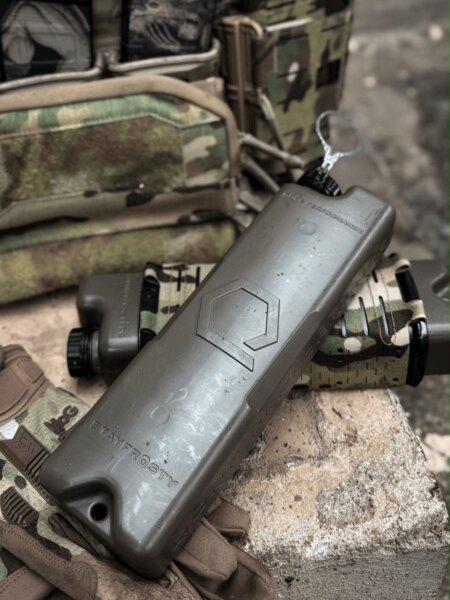 Qore Performance ICEFLASK<sup>&reg;</sup> placed next to a plate carrier and other tactical gear.