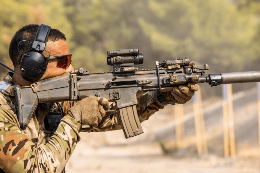Shooter with an FN SCAR rifle equipped with a red dot sight, weapon light, and suppressor.