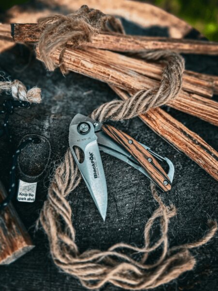 BlackFox folding knife with wooden handle scales resting on a chopping block beside kindling.