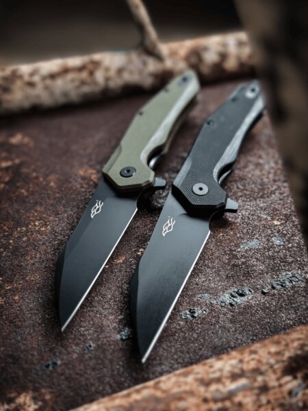 Two Ganzo folding knives with black-coated blades and handle scales in different colors.