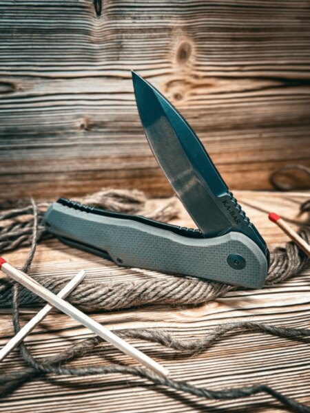 Ka-Bar folding knife on a wooden table with rope and matches.