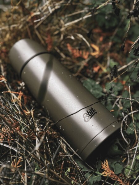 Esbit thermos lying among branches and forest vegetation.