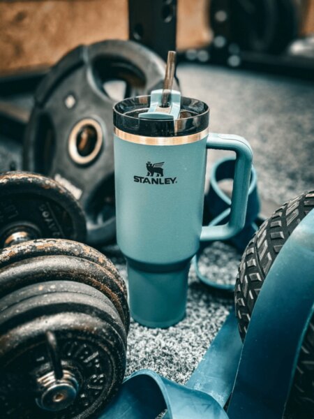 Stanley insulated tumbler with a straw placed among dumbbells and fitness equipment.