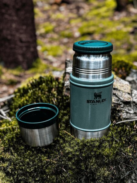 Open Stanley insulated food jar with its cup resting on moss in a forest.