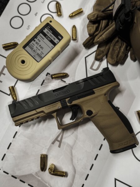Walther PDP Full Size handgun with a shot timer, ammunition and shooting gloves arranged on a target.