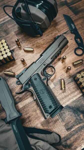 Schmeisser HUGO 1911 5" pistol in .45 ACP lying on a table with ammunition and shooting gear.