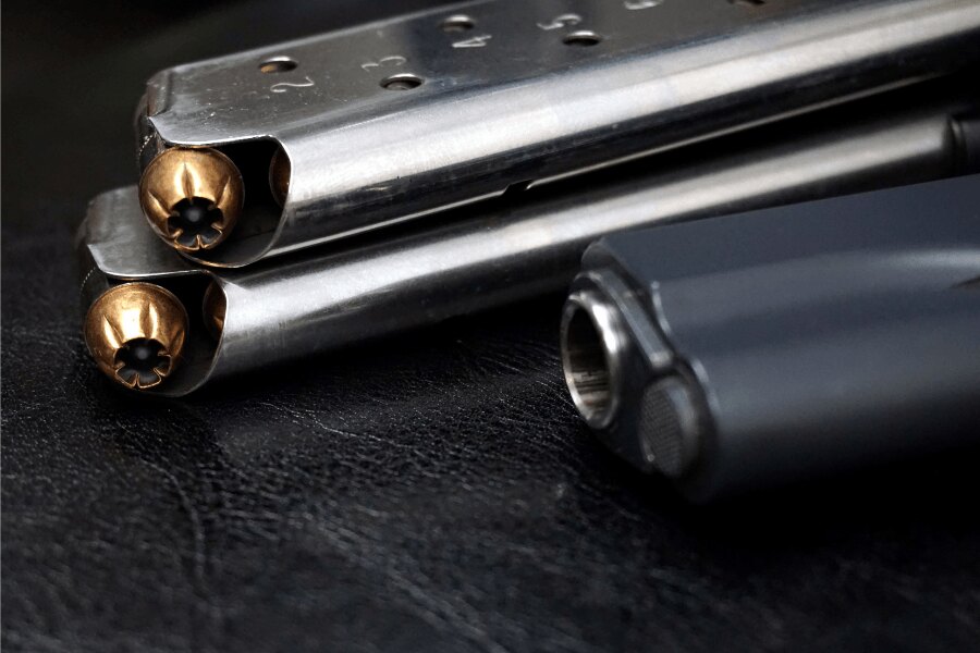 Close-up of M1911 magazines loaded with .45 ACP cartridges, with part of the pistol visible in the background.