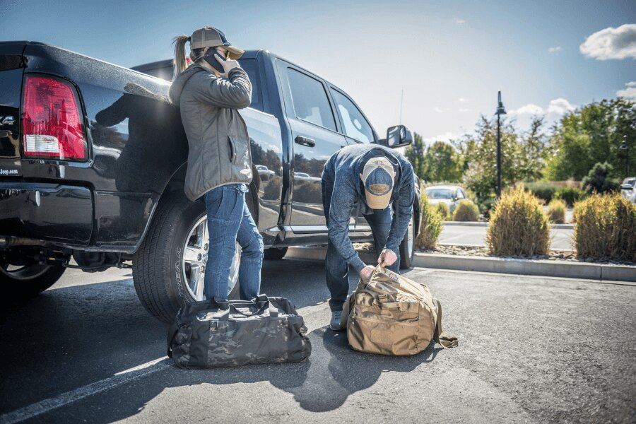 Two people preparing luggage next to a pickup truck before a journey.