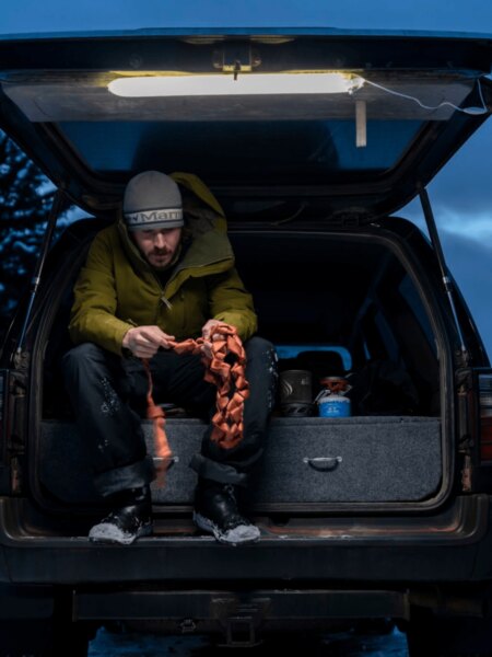Man sitting in the open trunk of a vehicle after dark under an auxiliary light.
