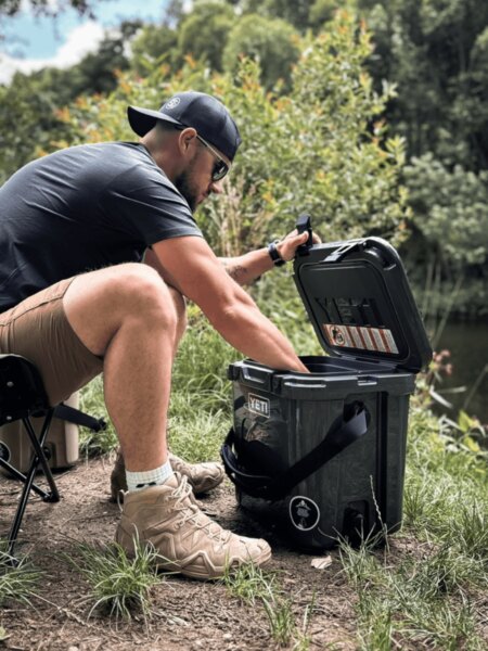 A man opening a YETI LoadOut GoBox near the water.