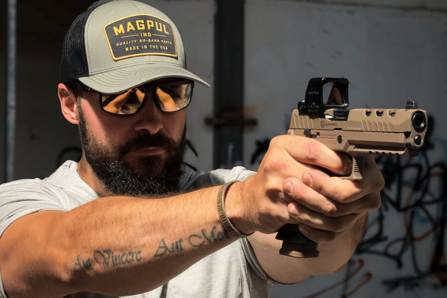 Shooter in protective glasses aims a SIG Sauer P320 DH3 pistol with a Holosun collimator.