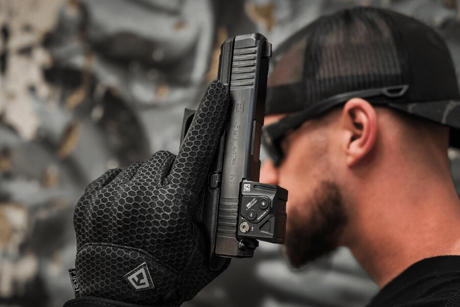 Close-up of a Glock 45 with a red dot sight held in a gloved hand.