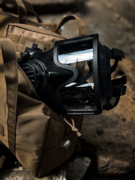 Close-up of an AVEC full-face protective mask with a panoramic lens resting on a backpack.