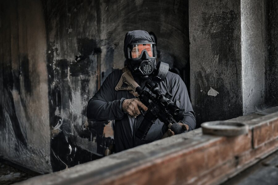 User wearing an AVEC full-face protective mask with a filter and carrying a rifle inside an industrial facility.
