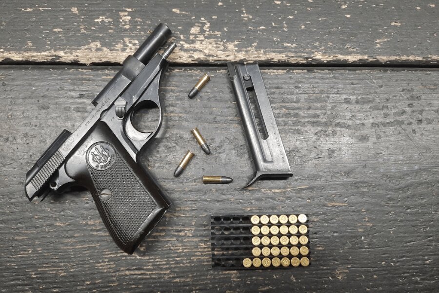 Beretta 71 pistol with its magazine removed and .22 LR cartridges on a dark wooden table.