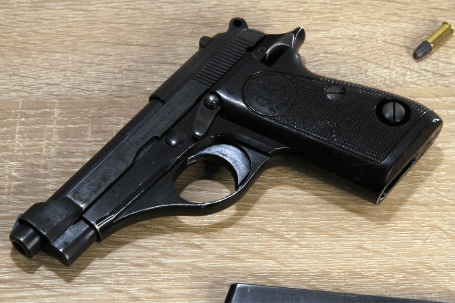 Close-up of a Beretta 71 pistol on a light wooden table.