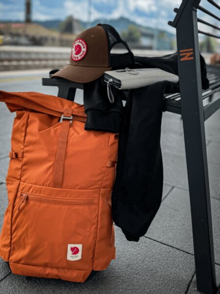Orange Fjällräven High Coast Foldsack 24 backpack leaning against a bench.