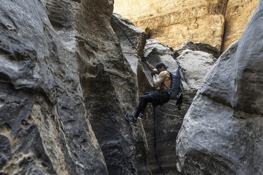 Man wearing a Klymit Splash 25 backpack while rappelling through a rocky canyon.