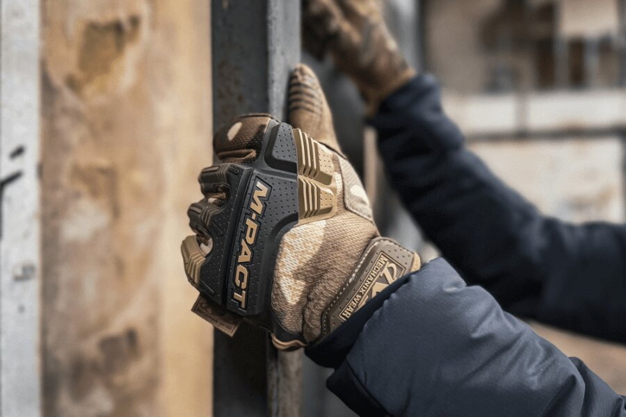 Hands wearing Mechanix M-Pact tactical gloves while gripping a metal structure.