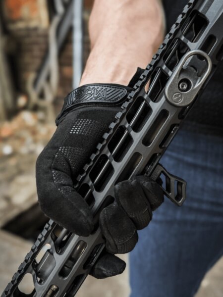 Hand wearing a black MoG Target Combat tactical glove while gripping a rifle handguard.