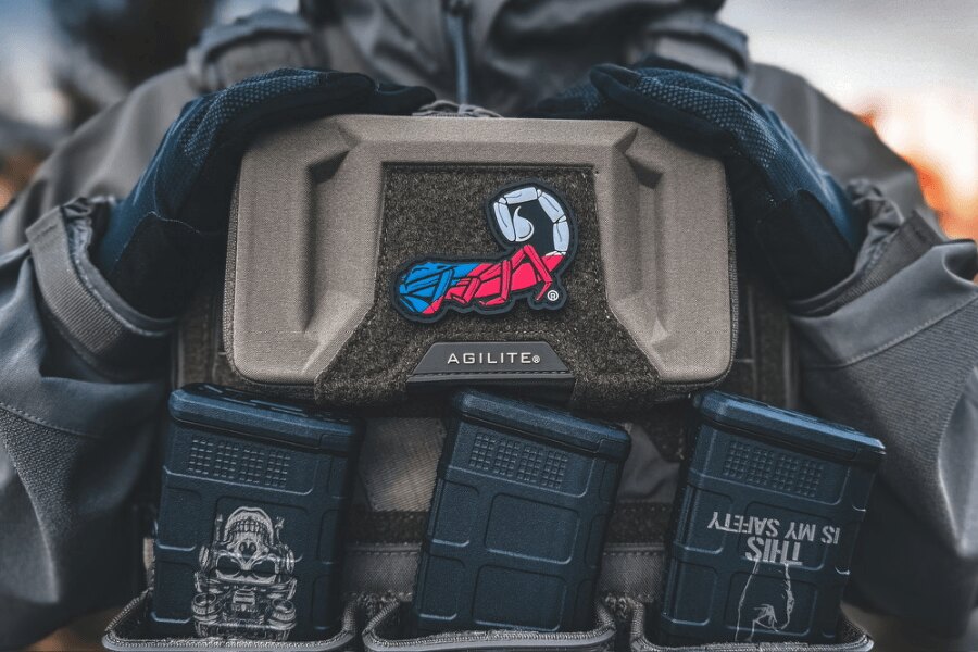 Close-up of the front panel of an Agilite plate carrier fitted with magazine pouches and a colorful scorpion patch.