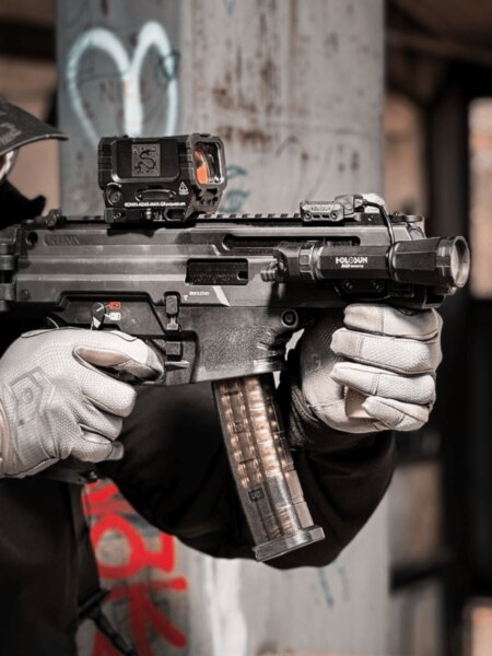Close-up of an HS Produkt KUNA fitted with a red dot sight, a side-mounted Holosun weapon light, and a translucent magazine.