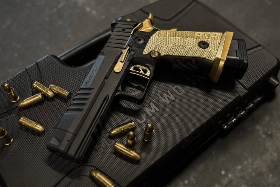 Black-and-gold SIG Sauer P211-GTO SPECTRE COMP pistol displayed on a hard case among cartridges.