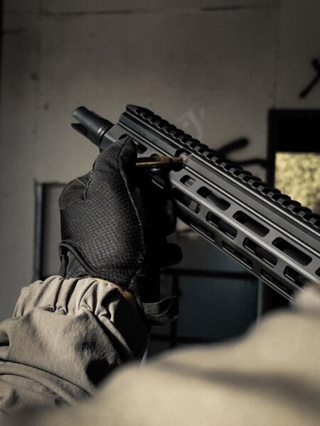 Close-up of the front end of an Antreg ARS M4s rifle, with a gloved hand holding a cartridge beside the handguard.