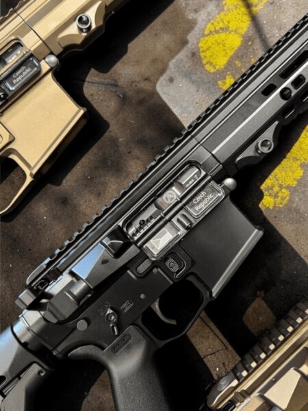 Three black and tan AR-15-pattern rifles arranged side by side on a concrete surface.